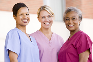 Three smiling nurses in three different color scrubs